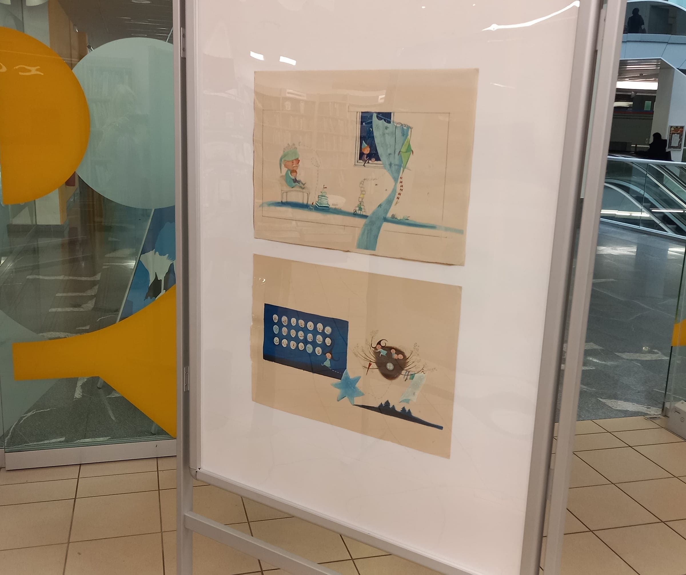 Razstavni pano z dvema ilustracijama iz slikanice Agica, mala čarovnica v TPC City, november 2024