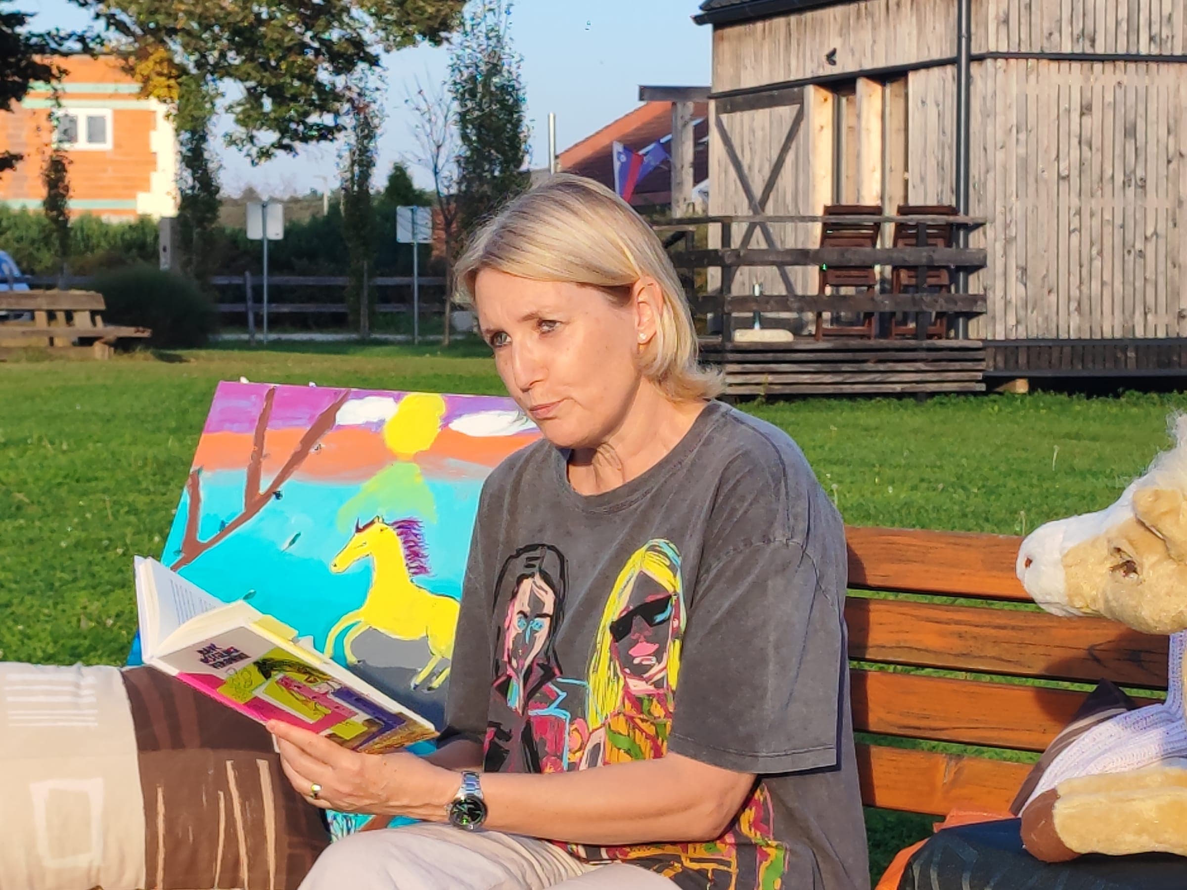Branje iz knjige na klopci na travniku, Konjeniški park Starošince, 2023