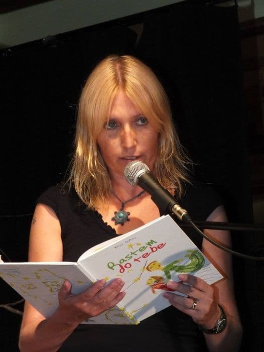 Bralka drži odprto knjigo Rastem do tebe in bere v mikrofon, Kulturno-gledališko društvo Reciklaža, 2015