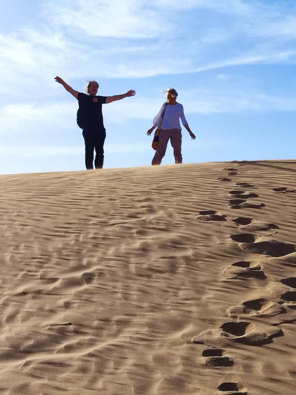 Veselo mahanje z vrha sipine, v pesku sledi stopinj, Festival pesnikov petih kontinentov, Laayoune, 2024